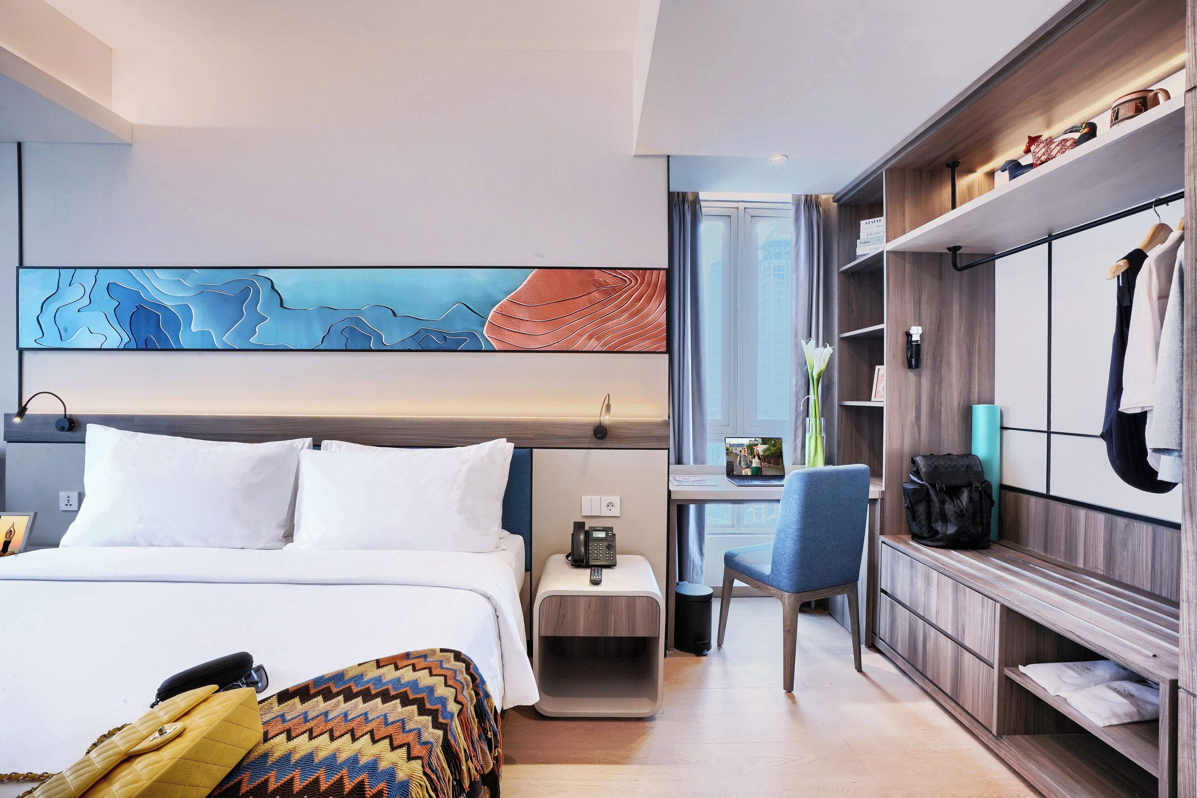 Un moderno cuarto de hotel con cama, escritorio, silla y un cuadro abstracto grande en la pared.