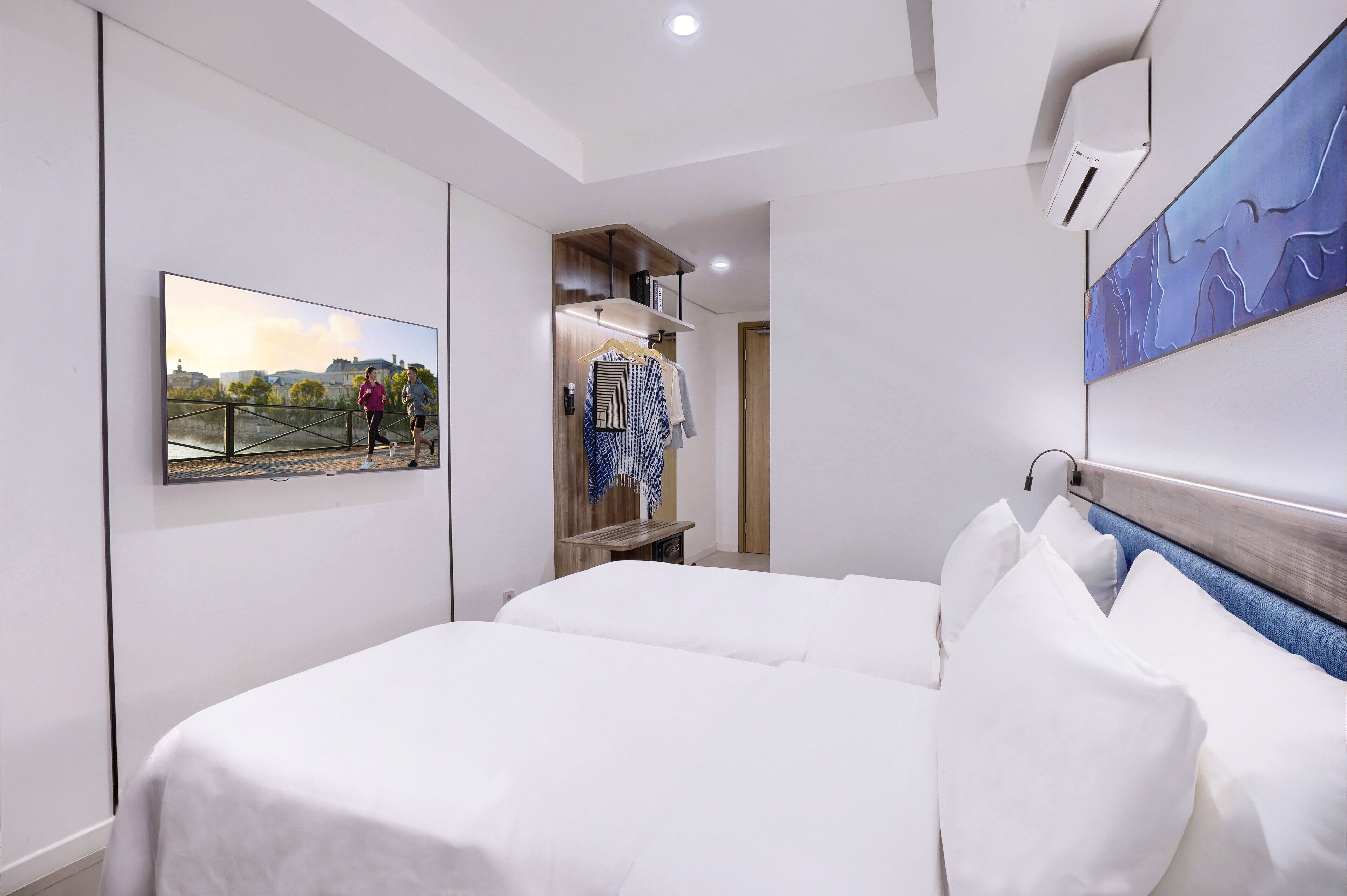 A hotel room with a bed, a TV mounted on the wall, a wardrobe, and a painting.