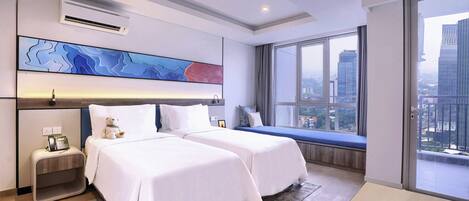 A modern hotel room with two beds, a large window with a city view, a mounted air conditioner, and a bedside table with a lamp.