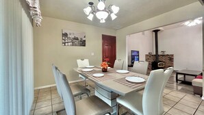 Een eetruimte met een lange tafel, stoelen, een vaas met bloemen, een open haard en een televisie.