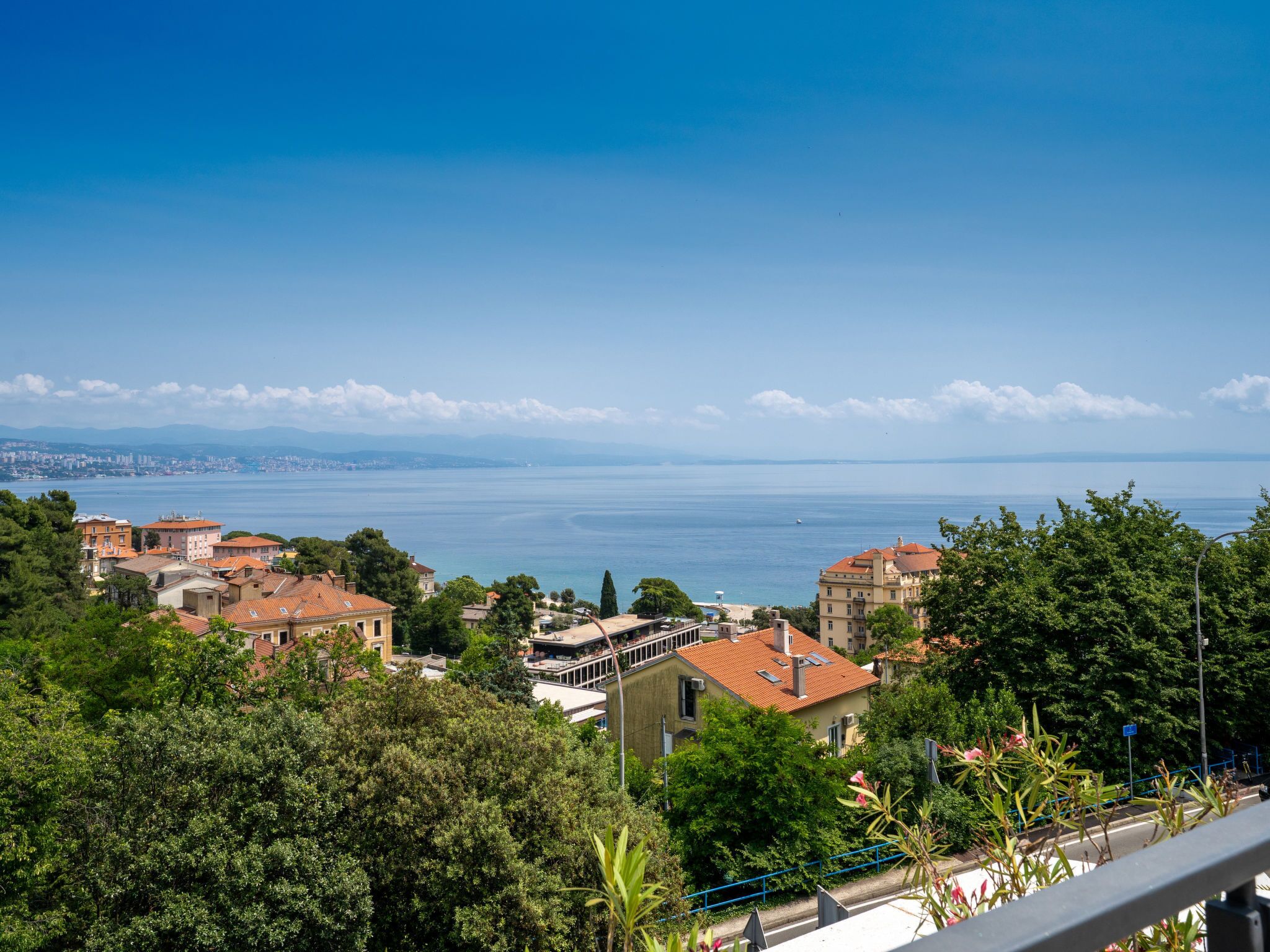 A coastal town with buildings overlooking the sea, a clear sky, and a distant city skyline.