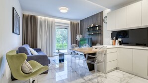 Un salon moderne comprenant un canapé, une table à manger avec des chaises, un coin cuisine avec des placards et une grande fenêtre agrémentée de rideaux.
