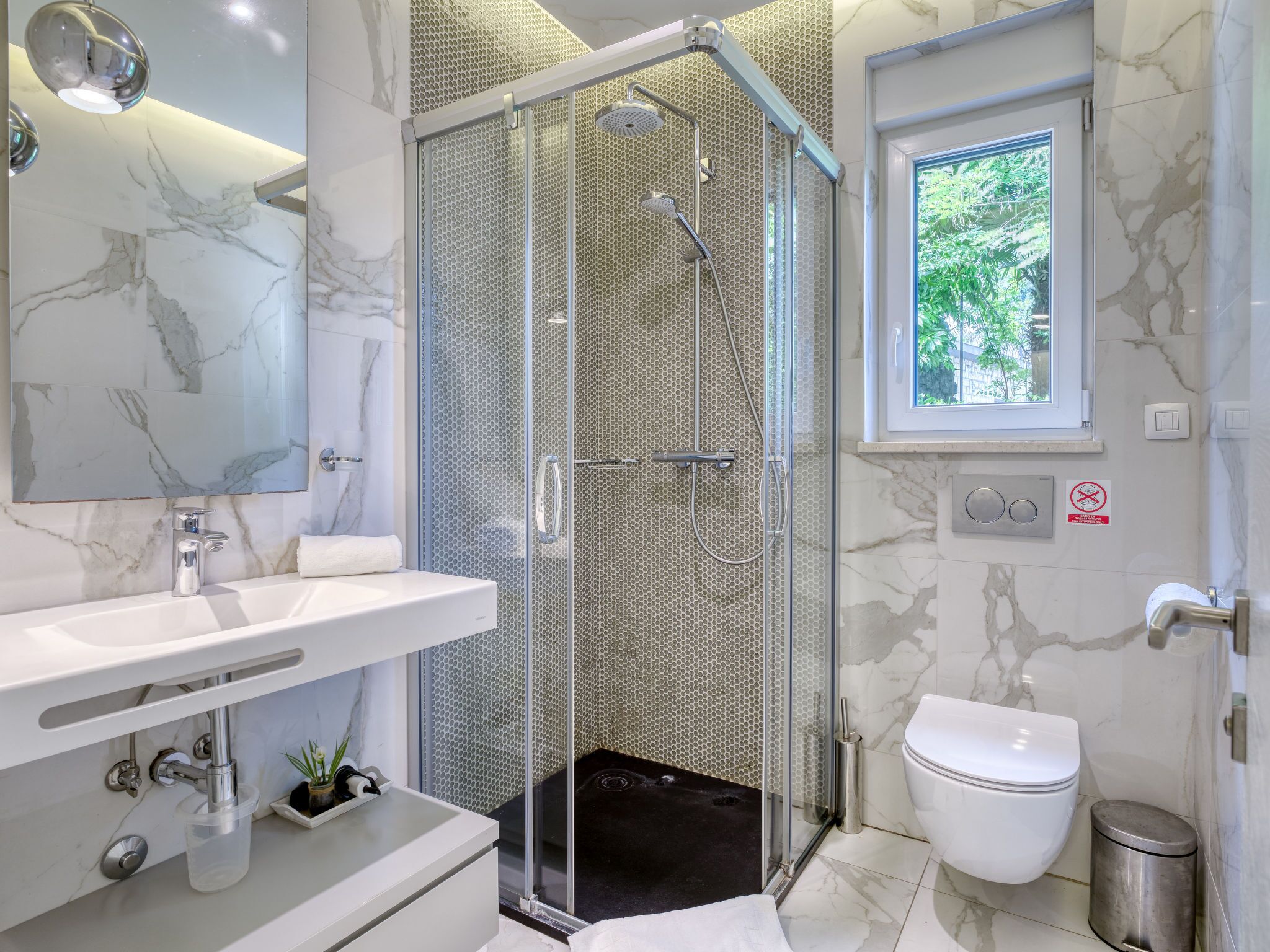 A modern bathroom with a glass-enclosed shower, a marble sink, and a toilet.
