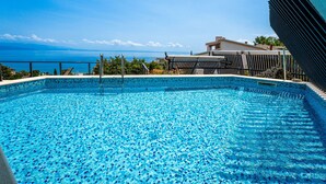 Une piscine d’un bleu éclatant, avec vue sur la mer et un bâtiment en arrière-plan.