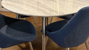 Una mesa de comedor redonda con tapa de mármol, rodeada por cuatro sillas azul oscuro con patas de metal.