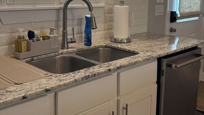 Una cocina con armarios blancos, un lavamanos de acero inoxidable y un lavavajillas integrado.