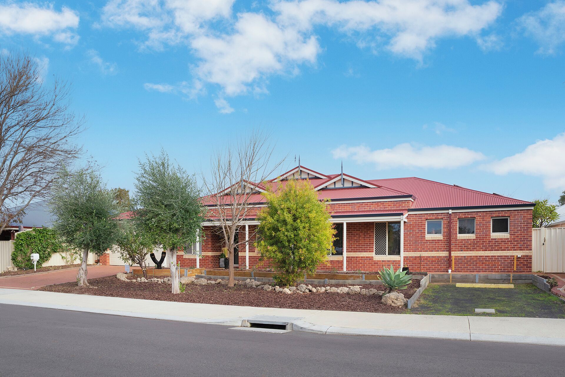 A two-story brick house with a red roof, a front porch, and a small front yard with landscaping.