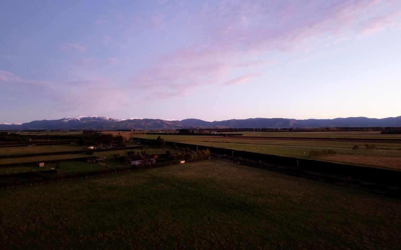 Paisagem rural com campos, um pequeno edifício e montanhas ao longe.
