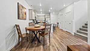Eine moderne Küche mit weißen Schränken, ein Essbereich mit einem Holztisch und -stühlen sowie eine Treppe, die zu einer weiteren Ebene führt.