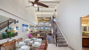 Un comedor amplio con una mesa de vidrio dispuesta para una comida, una escalera que sube a un nivel superior y vistas al exterior.