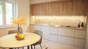 A modern kitchen with wooden cabinets, a round dining table with chairs, and a fruit bowl.
