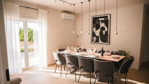 A dining area with a table set for six, chairs, a modern abstract painting, and an air conditioning unit.