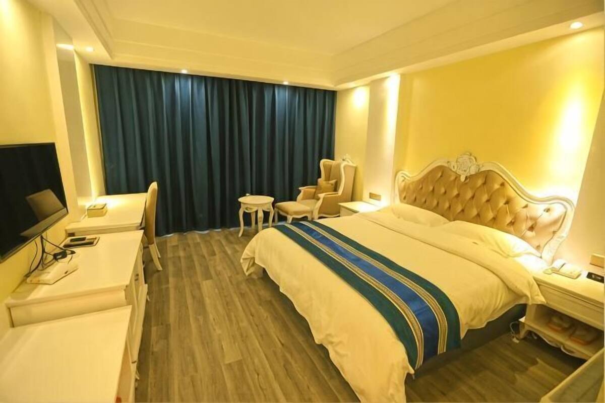 A hotel room with a bed, a desk, a chair, a small table, and a TV.