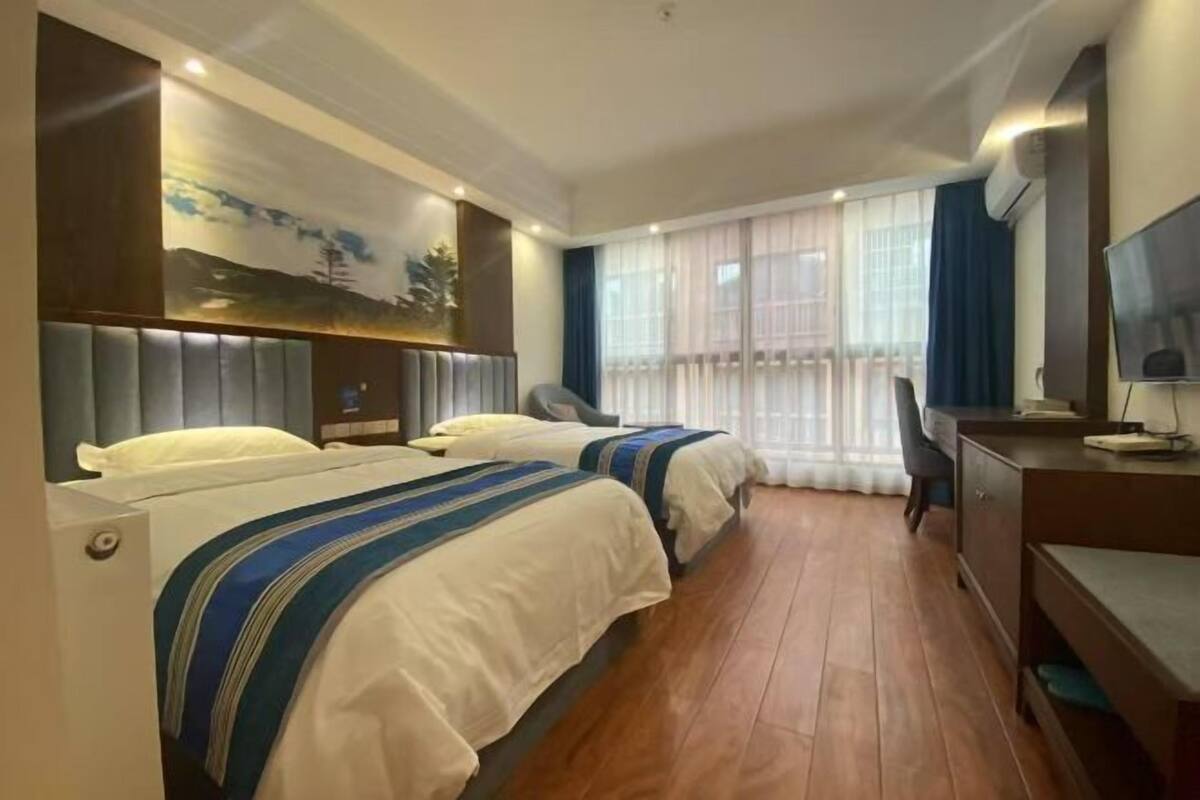 A hotel room with two beds, a desk, a chair, a TV, and a painting on the wall.
