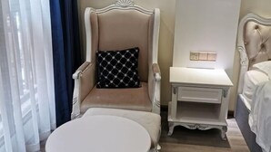 Hotellihuone, jossa on suuri nojatuoli, pieni yöpöytä ja pyöreä pöytä.