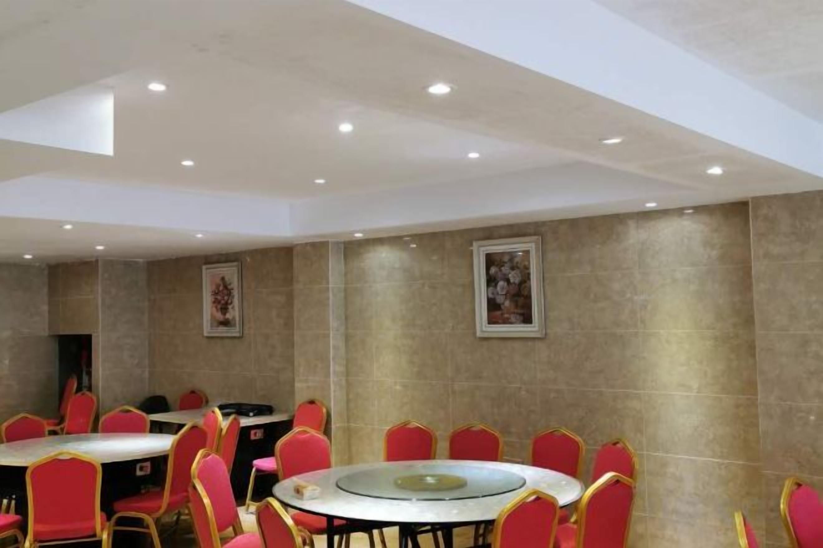A conference room with round tables and red chairs, equipped with ceiling lights.