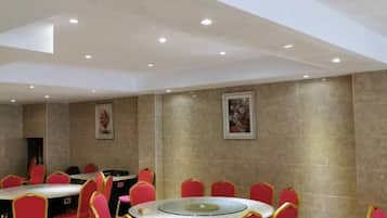 A conference room with round tables and red chairs, equipped with ceiling lights.
