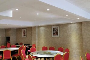 Une salle de conférence dotée de tables rondes et de chaises rouges, et équipée de luminaires encastrés au plafond.