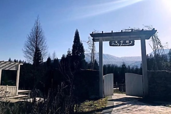 A wooden pergola with a sign, a stone wall, and a mountain in the background.