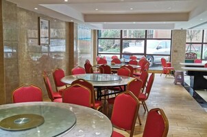 Um restaurante com mesas redondas e cadeiras vermelhas, janelas amplas e vista para o exterior.