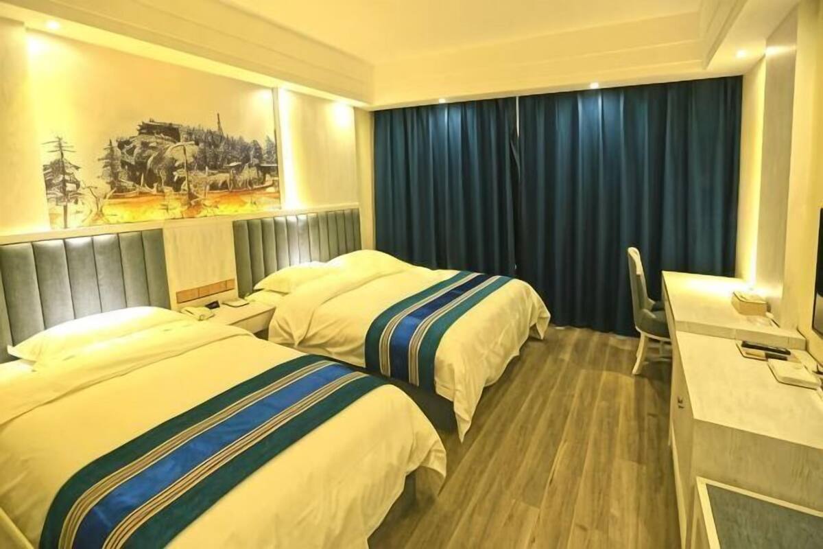 A hotel room with two beds, a desk, a chair, and a large window with curtains.