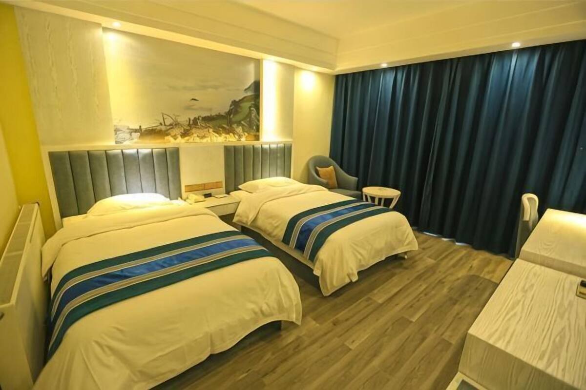 A hotel room with two beds, a desk, a chair, a small table, and a large window with curtains.