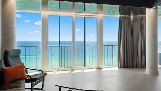 Een ruime kamer met een grote schuifglazen deur die leidt naar een balkon met uitzicht op de oceaan.