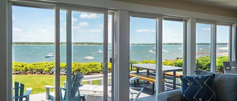 A room with large sliding glass doors leading to an outdoor deck with a view of the water and boats.