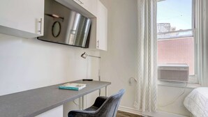 A compact room with a grey countertop, a chair, a small table, a mirror, and a window with a view of a brick building.