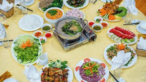A table set with various dishes, including rice, noodles, and meat, with a hot pot in the center. - Golden Mountain Hostel  (Ninh Binh)