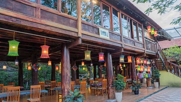 A wooden building with a balcony, labeled "DORM 2," featuring outdoor seating with tables and chairs, potted plants, and hanging lanterns. - Golden Mountain Hostel  (Ninh Binh)