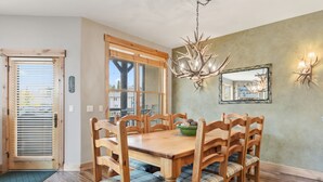 A dining area with a wooden table and chairs, a chandelier, and a wall-mounted mirror. - Walk to Main Street | Hot Tub, Gym and Game Room (Breckenridge)