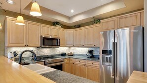 A modern kitchen with wooden cabinets, a stainless steel refrigerator, a microwave, and granite countertops. - Walk to Main Street | Hot Tub, Gym and Game Room (Breckenridge)