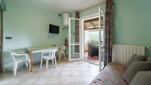 A room with a bed, a table with chairs, a TV, and a sliding glass door leading to an outdoor area.