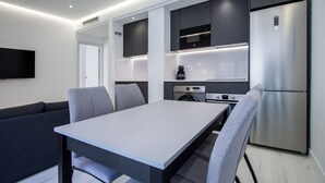 A modern kitchen with a dining table, chairs, built-in appliances, and a flat-screen TV.