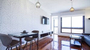 A modern living room with a glass dining table, two chairs, a sofa, and a TV mounted on the wall. - CASTELLANA PARKING 1 BEDROOM - 02 (Madrid)