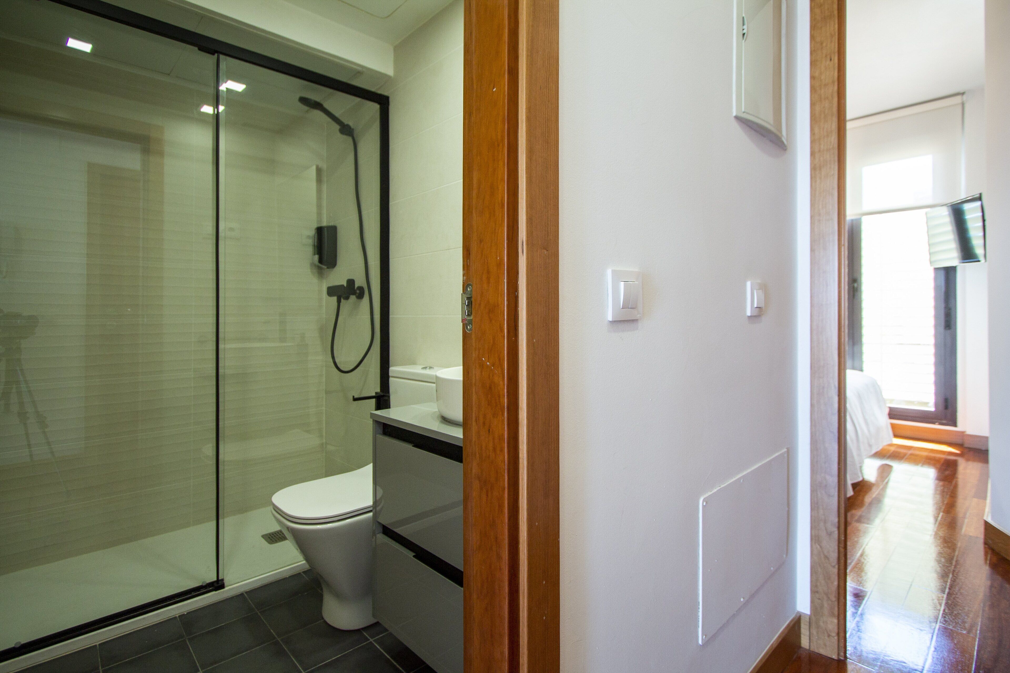 Un baño moderno con cabina de ducha de vidrio, un inodoro blanco y un marco de puerta de madera.