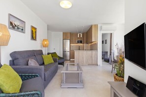 Sala de estar moderna com sofá cinzento, mesa de centro transparente e televisão de tela plana.