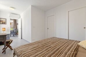 A bedroom with a bed, a desk, and a chair in a bright room with white walls and a door. - Torre Mar - Playamar (Torremolinos)