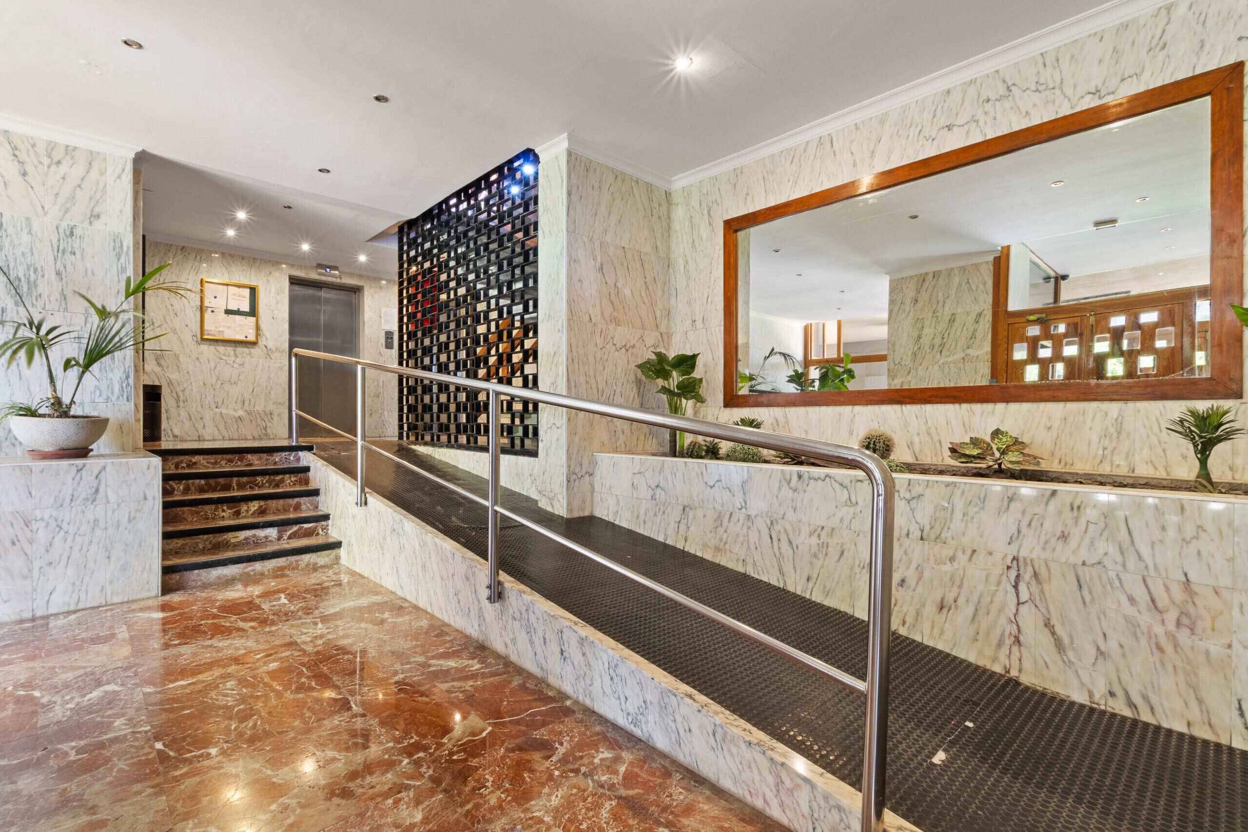 Escadaria com piso de mármore, corrimão, espelho fixado na parede e painel decorativo.