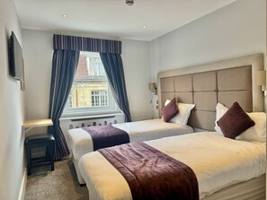 Ein Hotelzimmer mit zwei Betten, einem Schreibtisch und einem Fenster mit Vorhängen.