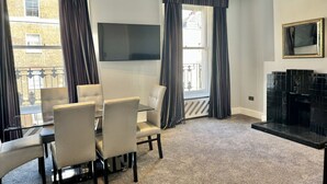 A modern living room with a dining area, large windows with curtains, a flat-screen TV, and a fireplace. - 2 Bed/3 Bath Brand New Modern Flat with Air Con (Greater London)