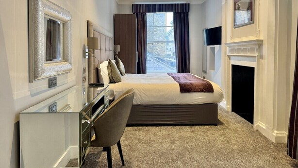 A hotel room with a bed, a desk, a chair, a fireplace, and a large window with curtains. - 2 Bed/3 Bath Brand New Modern Flat with Air Con (Greater London)