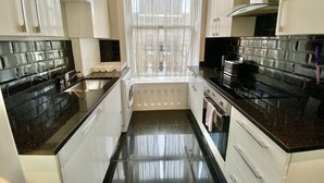 A compact kitchen with black countertops, white cabinets, and a window with sheer curtains. - 2 Bed/3 Bath Brand New Modern Flat with Air Con (Greater London)