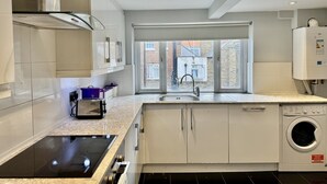 A modern kitchen with a built-in stove, a washing machine, and a window with a view of the city.