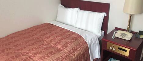 A neatly made bed with a patterned bedspread, a white pillow, and a wooden nightstand with a lamp and a telephone.
