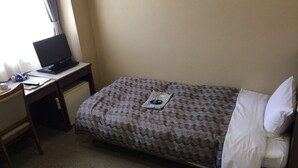 Ein kleines, ordentlich eingerichtetes Schlafzimmer mit einem Einzelbett, einem Schreibtisch mit Computer und einem Stuhl.
