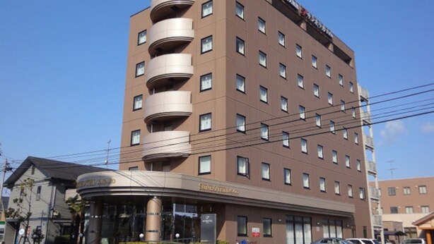 Ein mehrstöckiges Hotel mit geschwungenem Eingang, Balkonen und einem Parkplatz mit Autos.