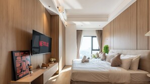 A modern hotel room with a large bed, a flat-screen TV mounted on the wall, and a window with curtains. - Vue Aston Condominium by Soben Homes (Phnom Penh)