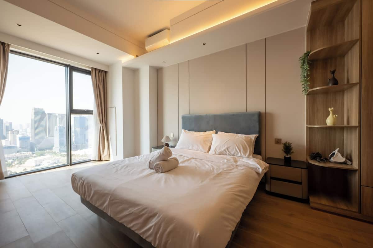 Ein modernes Hotelzimmer mit einem großen Bett, einem Nachttisch, einem Holzregal und Blick auf die Stadt.